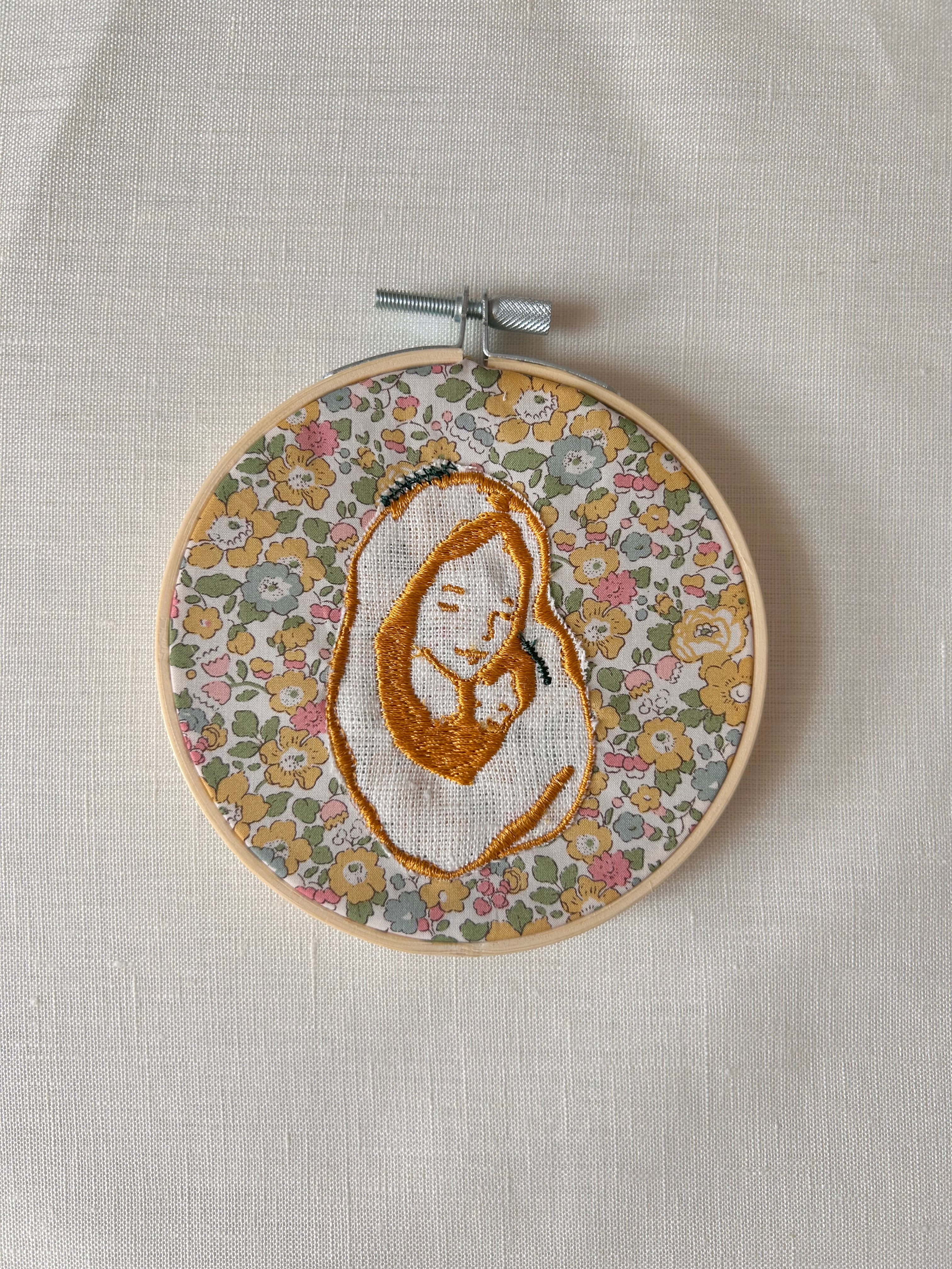 Virgen bordada sobre tela de color amarillo sobre flores